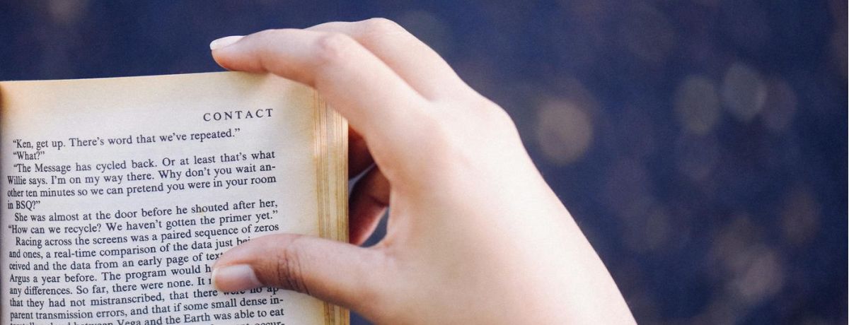 person reading a book indoors, with hand on book