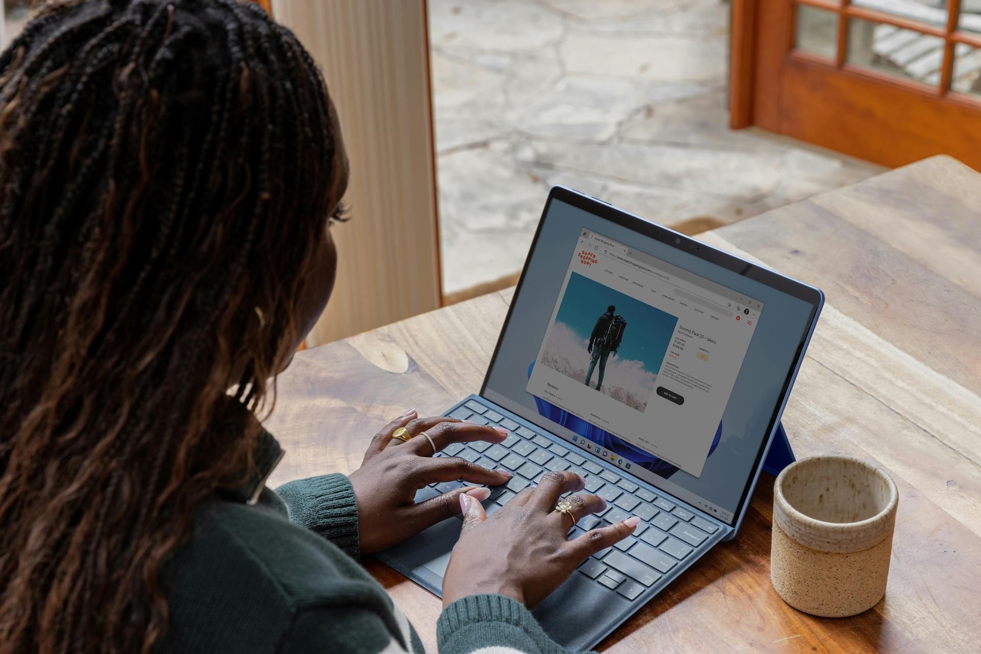 woman using a computer on a table with a mug next to the laptop