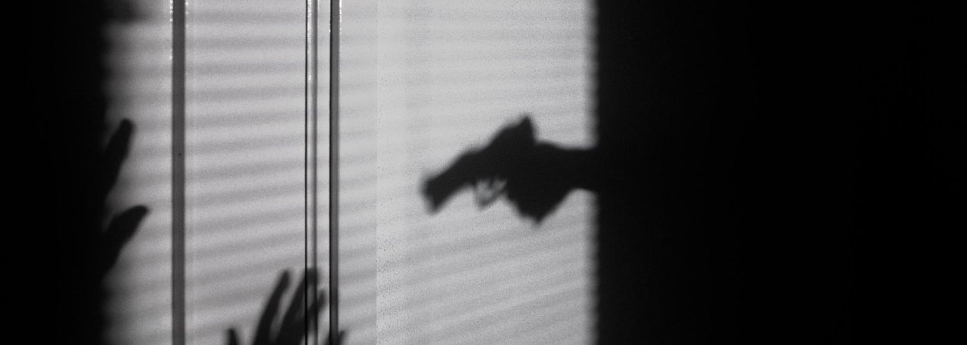 shadow on blinds of a person holding a gun towards a victim