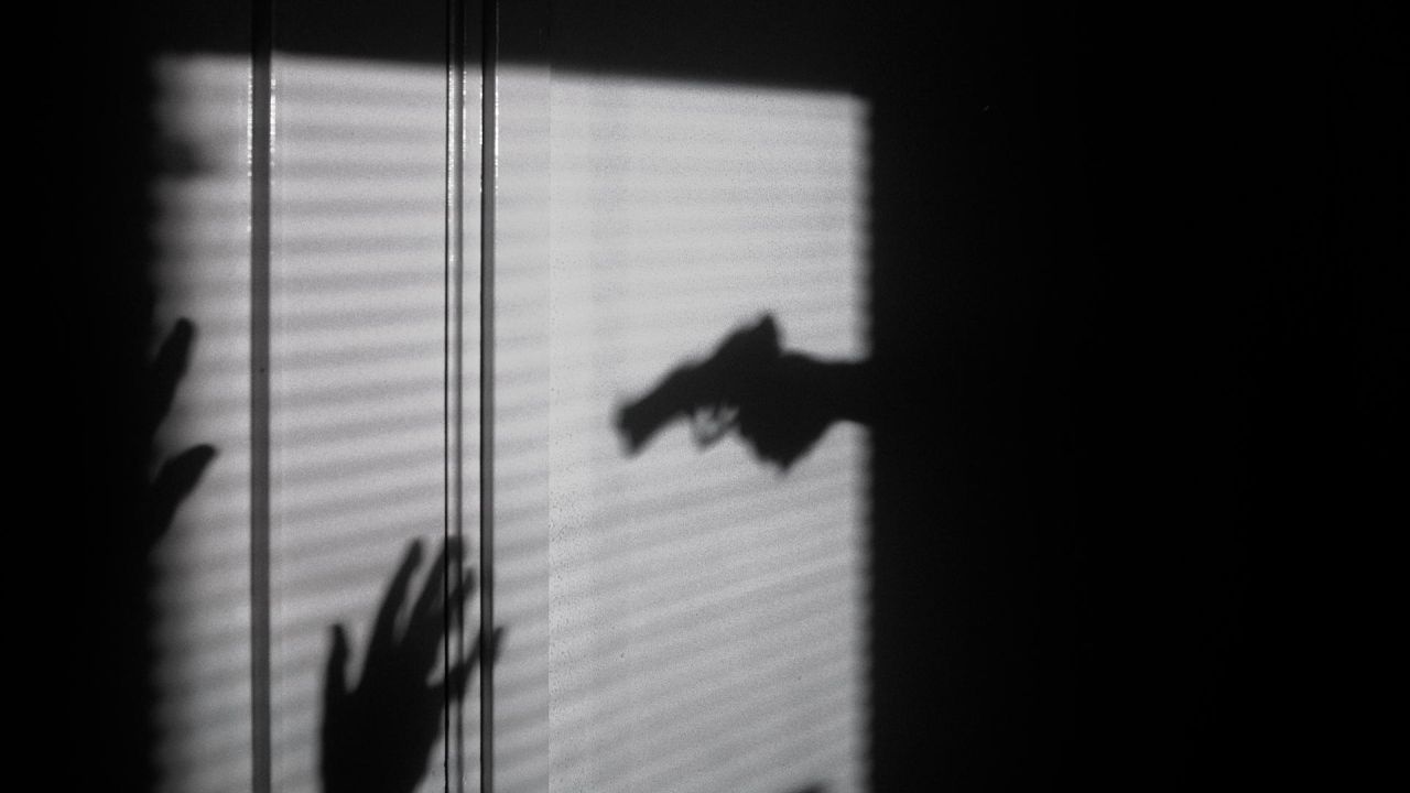 shadow on blinds of a person holding a gun towards a victim