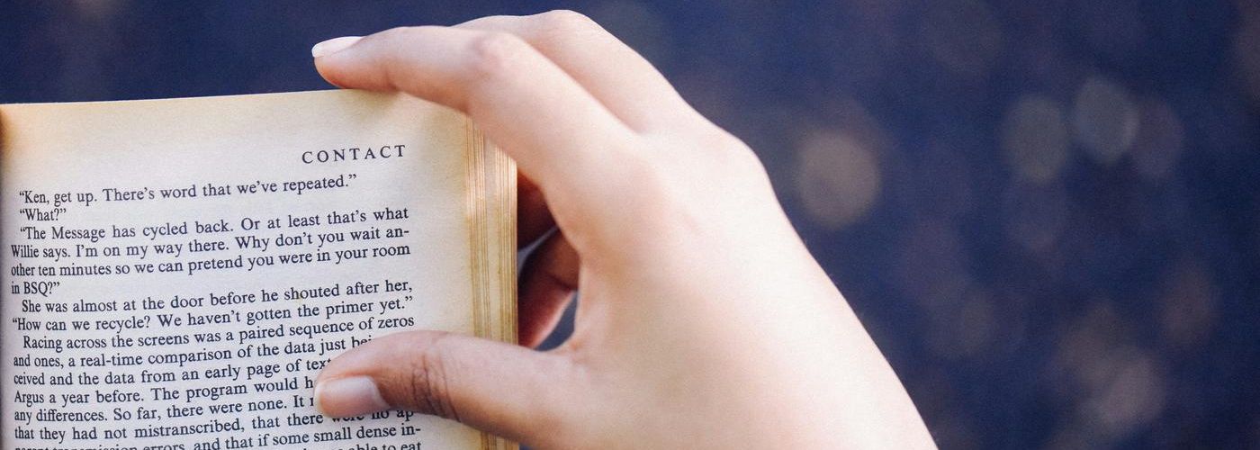 person reading a book indoors, with hand on book