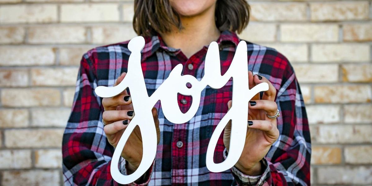 A picture of a woman, outside, holding a joy sign