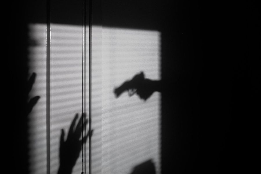 shadow on blinds of a person holding a gun towards a victim